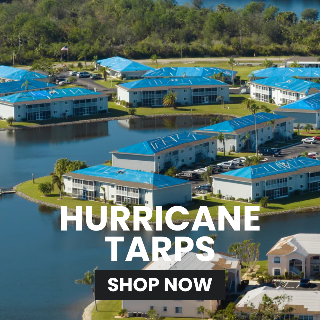 Aerial view of buildings with blue hurricane tarps over windows, surrounded by water and greenery.