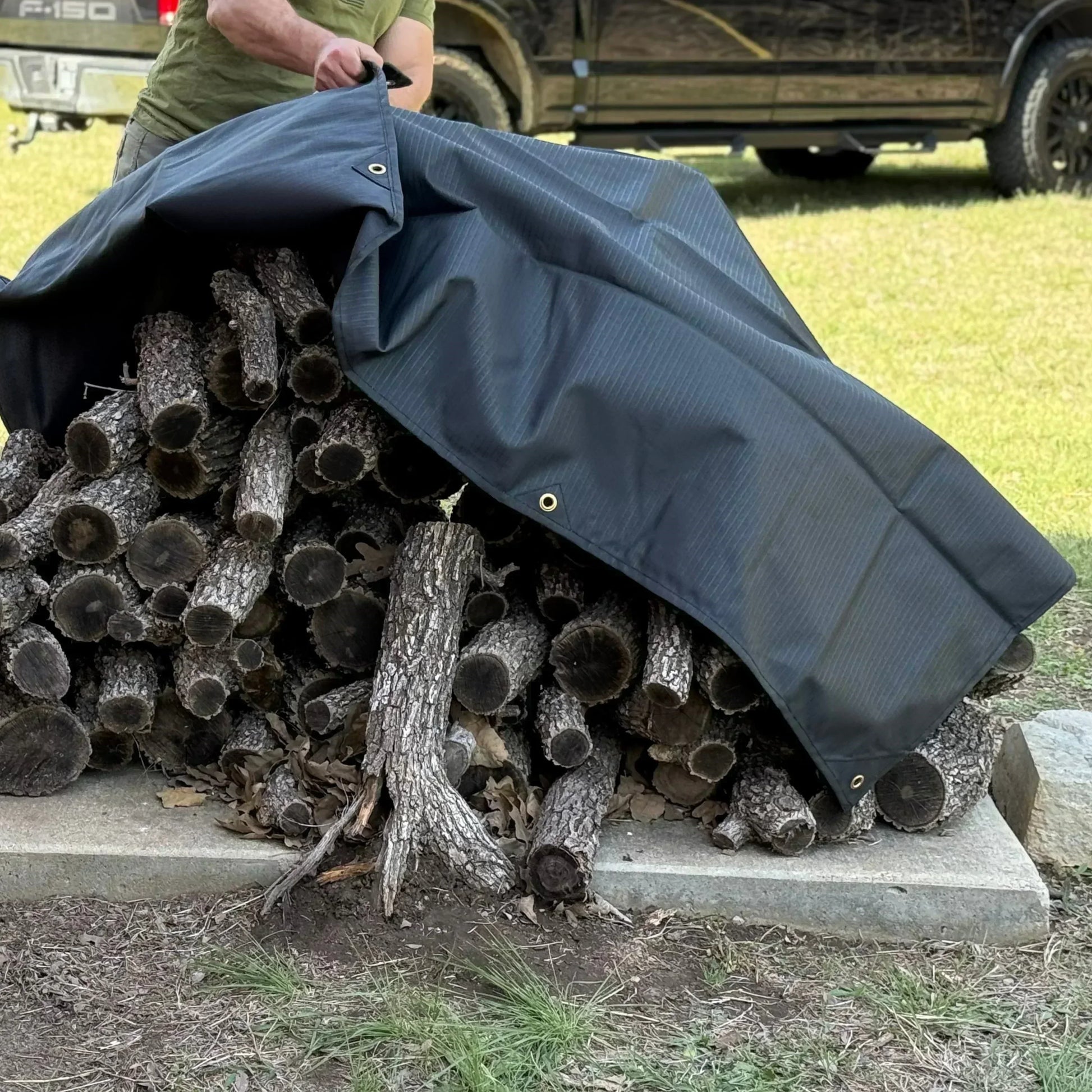 Black 10' x 10' waterproof canvas tarp protecting stacked firewood from rain exposure