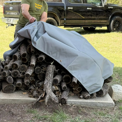 Gray 14' x 20' waterproof canvas tarp shielding stacked logs from weather exposure