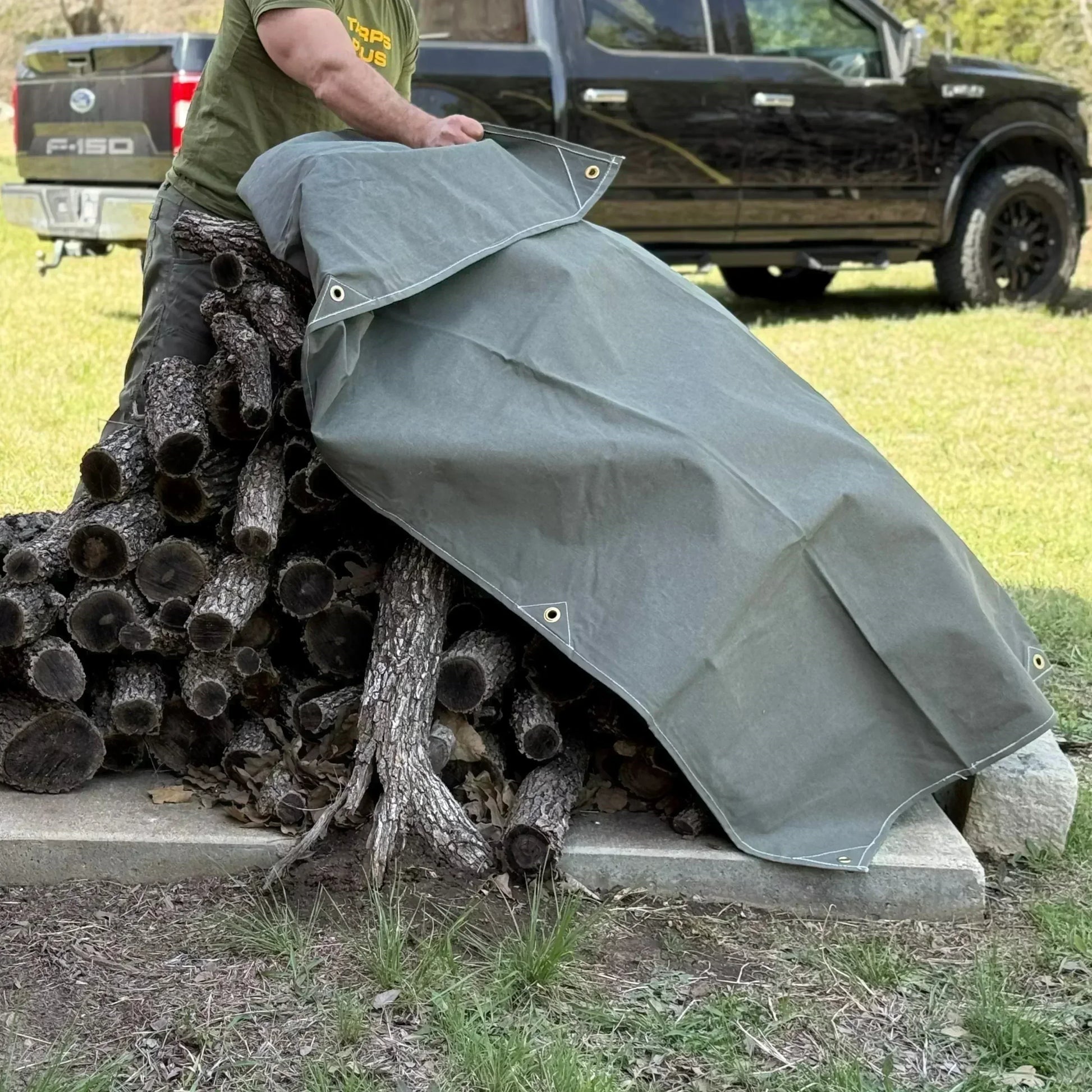 Olive Drab 20' x 20' fire retardant canvas tarp shielding stacked logs from exposure conditions