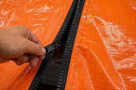 Close-up of black tarp zipper installed on orange poly tarp showing hand opening zipper entrance