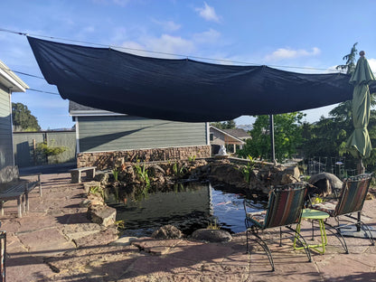 Black 86% super shade mesh tarp installed above a backyard pond and patio area; provides cooling shade and UV protection while allowing airflow and light.